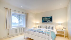 A bedroom with a bed, a window with curtains, a radiator, a bedside table, and a wall-mounted painting. - 2 Bed in Swanage (oc-t34732) (Swanage)