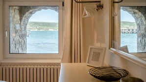A room with two windows framed by stone arches, a radiator, a small table with a picture frame, and a mirror. - 2 Bed in Swanage (oc-t34732) (Swanage)