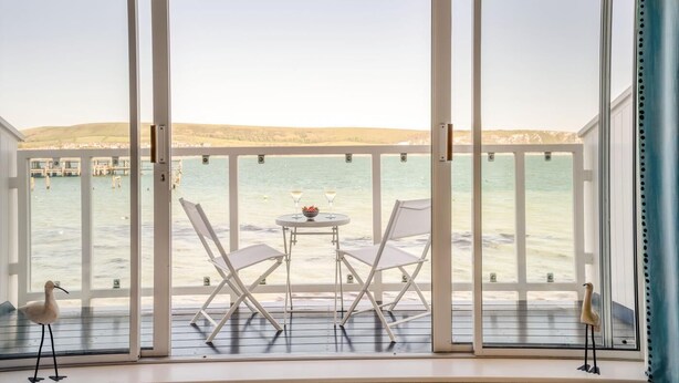 A balcony with a table and chairs, overlooking a body of water and a distant shoreline. - 2 Bed in Swanage (oc-t34732) (Swanage)