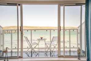 Een balkon met een tafel en stoelen, met uitzicht op een wateroppervlak en een verre kustlijn.