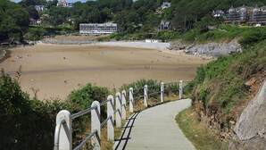 A beach with a pathway leading to the shore, surrounded by greenery and buildings. - 4 Bed in Gower (oc-hh672) (Horsham)