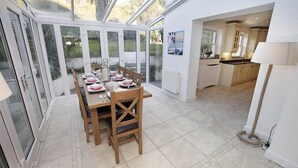 A dining area with a table set for four, a kitchen in the background, and a view through large glass doors. - 4 Bed in Gower (oc-hh672) (Horsham)