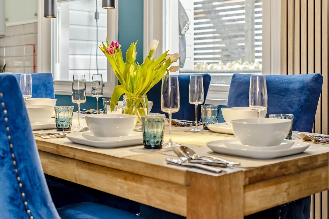 Ein Esstisch, gedeckt mit weißen Tellern, blauem Glas und einer Blumenvase.