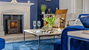 En stue med pejs, en blå sofa, en træstol, et bord med blomster i en vase og et ur på pejsen.
