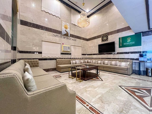 Um hall de hotel com área de estar, um candelabro, uma televisão e um balcão de recepção.