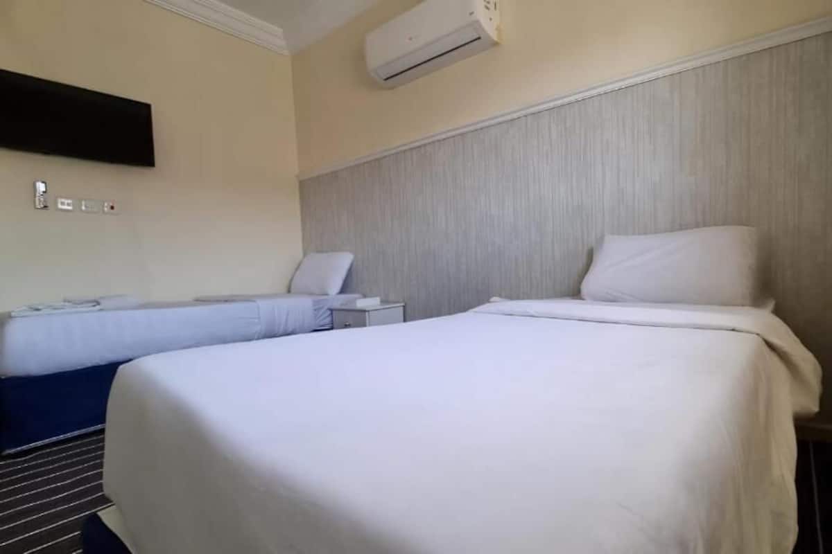 Quarto de hotel com duas camas, uma TV de tela plana, ar condicionado e uma mesa de cabeceira com abajur.