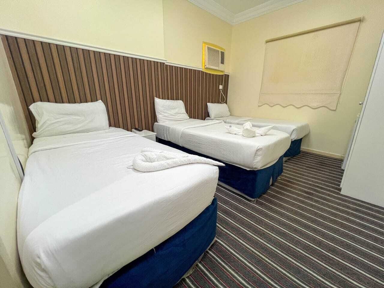 Una habitación de hotel con dos camas, alfombra a rayas, cabecera de madera y una ventana con persiana.