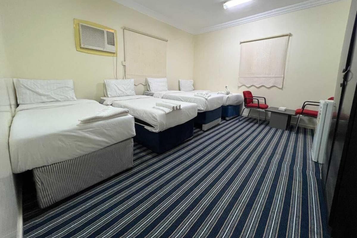 Quarto de hotel com três camas, uma escrivaninha e uma cadeira.