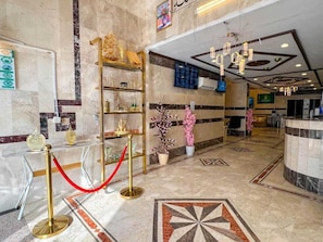 Um hall de hotel com piso de mármore, um balcão de recepção, uma mesa de recepção dourada e uma barreira de corda vermelha.