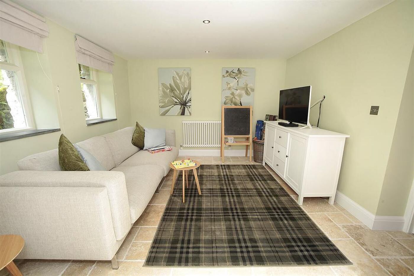 Ein Wohnzimmer mit einer Couch, einem kleinen Tisch, einem karierten Teppich, einer Heizung, einem Fernseher und Bildern an den Wänden.