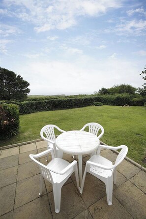 A patio with a round table and four chairs, surrounded by a well-maintained lawn and hedges. - 4 Bed in Gower (oc-hh45) (Pilton Rhossili)