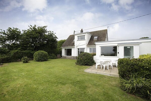 A two-story house with a well-maintained lawn, a patio with chairs, and a large window overlooking the garden. - 4 Bed in Gower (oc-hh45) (Pilton Rhossili)
