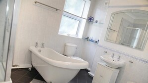Un baño con bañera tipo patas de león, inodoro, lavamanos y espejo.