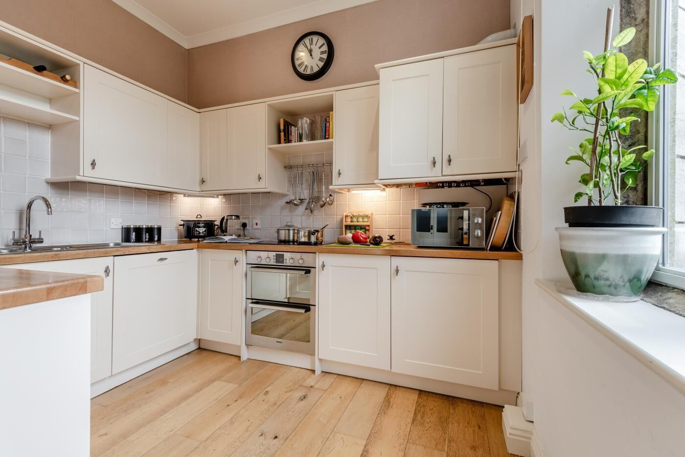 A kitchen with white cabinets, a wooden countertop, a built-in oven, and a clock on the wall.