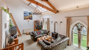 Ein großzügiges Wohnzimmer mit Kamin, Ledersofas, einer Holztreppe und einem großen Fenster mit Buntglas.