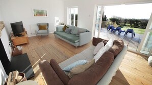 Ein Wohnzimmer mit einer Couch, einem Fernseher, einem Couchtisch und Blick ins Freie.
