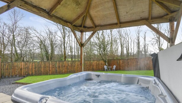 A hot tub under a wooden pergola in a backyard with a wooden fence and chairs. - 2 Bed in Newchapel (oc-c34717) (Clydau)