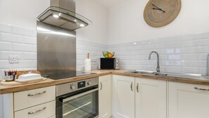 A modern kitchen with white cabinets, a stainless steel range hood, a built-in oven, a microwave, a sink, and a clock on the wall. - 2 Bed in Newchapel (oc-c34717) (Clydau)