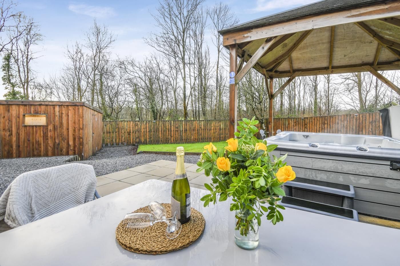 A patio area with a hot tub, a covered seating area, and a table with a bottle and glasses.