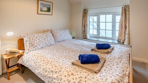 Quarto com cama, mesa de cabeceira, abajur, janela com cortinas e um quadro na parede.