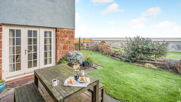 A house with a stone exterior, a wooden deck, and a garden with a view of the sea. - 3 Bed in Dunbar (oc-k34653) (Dunbar)