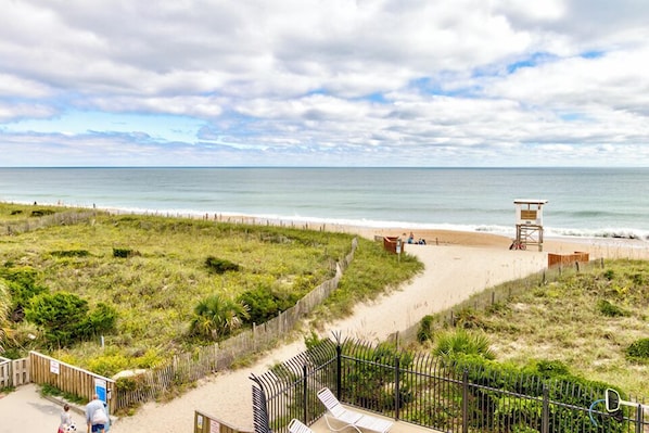 A beach view with a wooden fence, a lifeguard tower, and a sandy path leading to the water. - Ocean Views, Balcony, Pool,  STEPS to Beach Restaurants Shops (Wrightsville Beach)