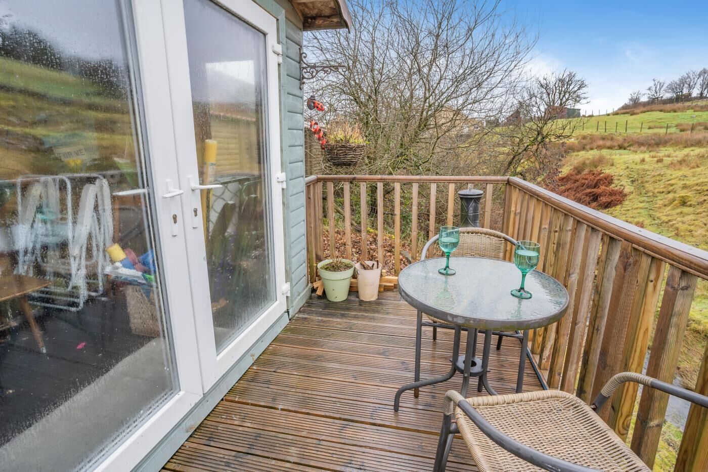 Une terrasse en bois avec une porte vitrée, une table ronde entourée de chaises et des plantes en pot.