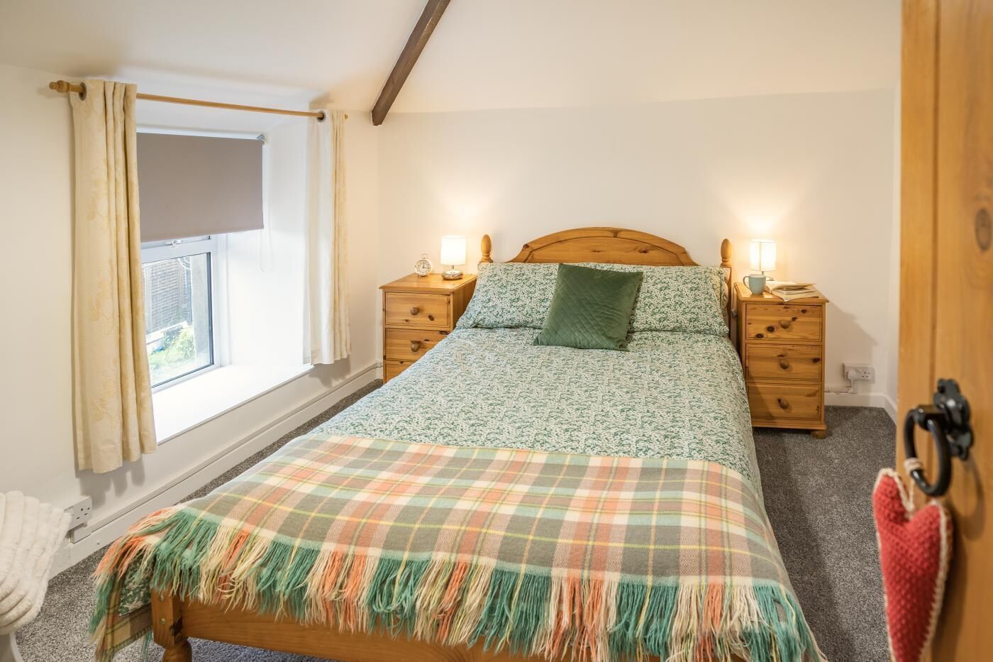 Une chambre à coucher avec un lit, deux tables de chevet, une fenêtre avec des rideaux, une tête de lit en bois et une décoration en forme de cœur rouge.
