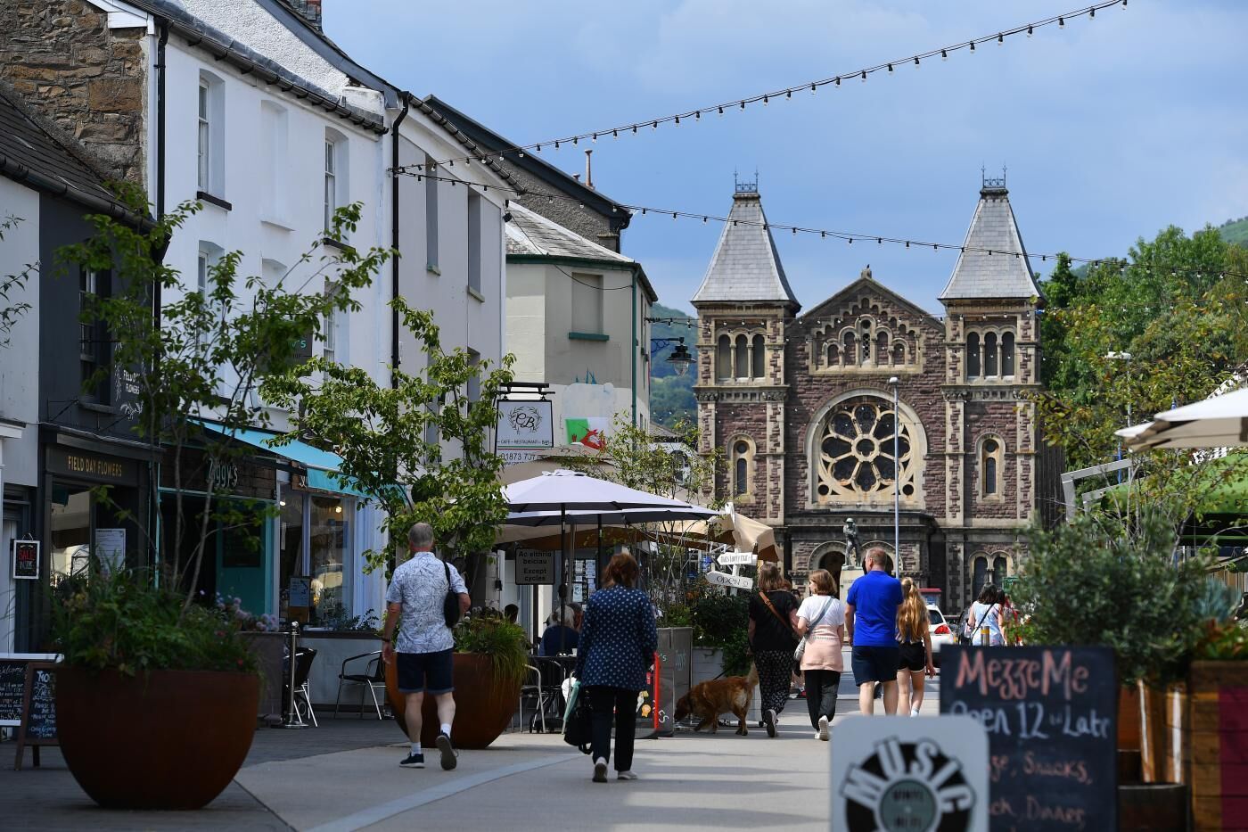 A street with pedestrians, a historic church, and outdoor seating areas.