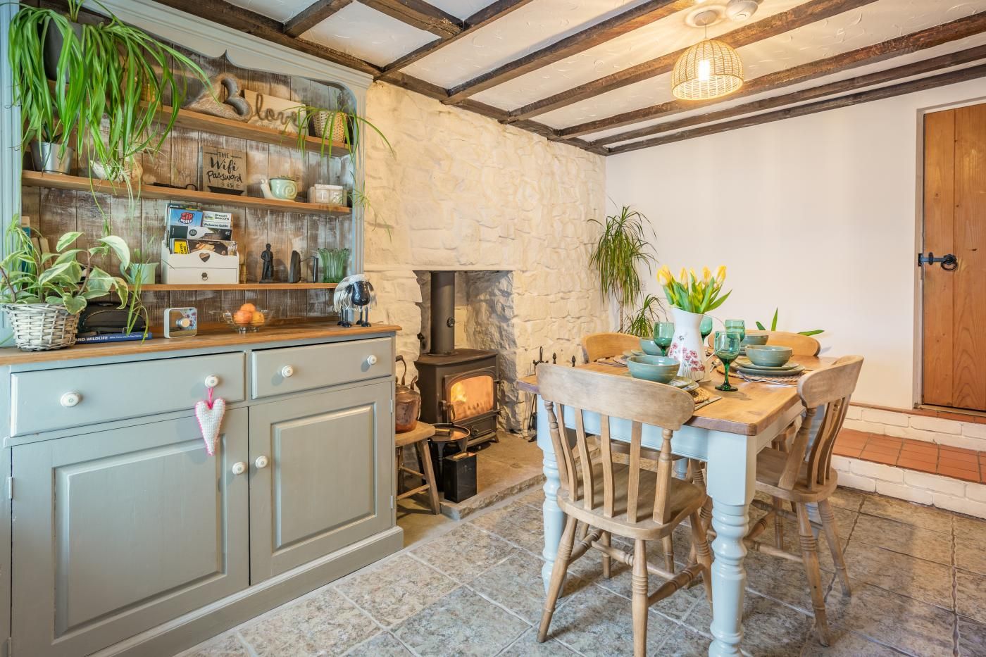 Une cuisine rustique avec un mur en pierre, des poutres en bois, un poêle et une table à manger dressée pour deux personnes.