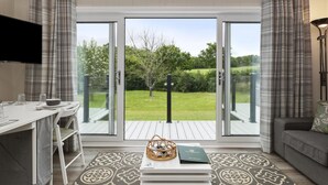 Una sala de estar moderna con comedor, un sofá, un televisor y vistas a un jardín a través de puertas de cristal.