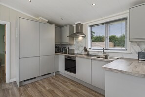 A modern kitchen with built-in appliances, a window with blinds, and a light-colored floor.
