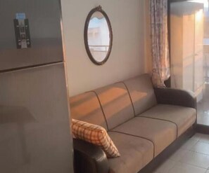 A living area with a sofa, a mirror, and a window with curtains. - Γκαρσονιέρα καινούρια στον Άγιο Ιωάννη καλαμριας (Thessaloniki)