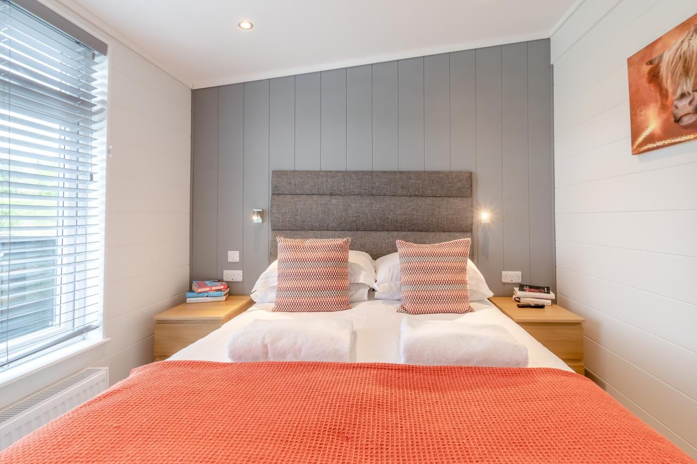 Ein modernes Schlafzimmer mit einem großen Bett, zwei Nachttischen und einem Fenster mit Jalousien.