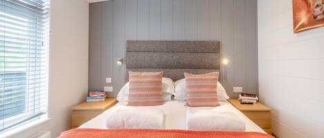 Ein modernes Schlafzimmer mit einem großen Bett, zwei Nachttischen und einem Fenster mit Jalousien.