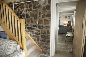A staircase with a wooden handrail leading to a stone wall, a striped sofa, and a dining area with a table and chairs.