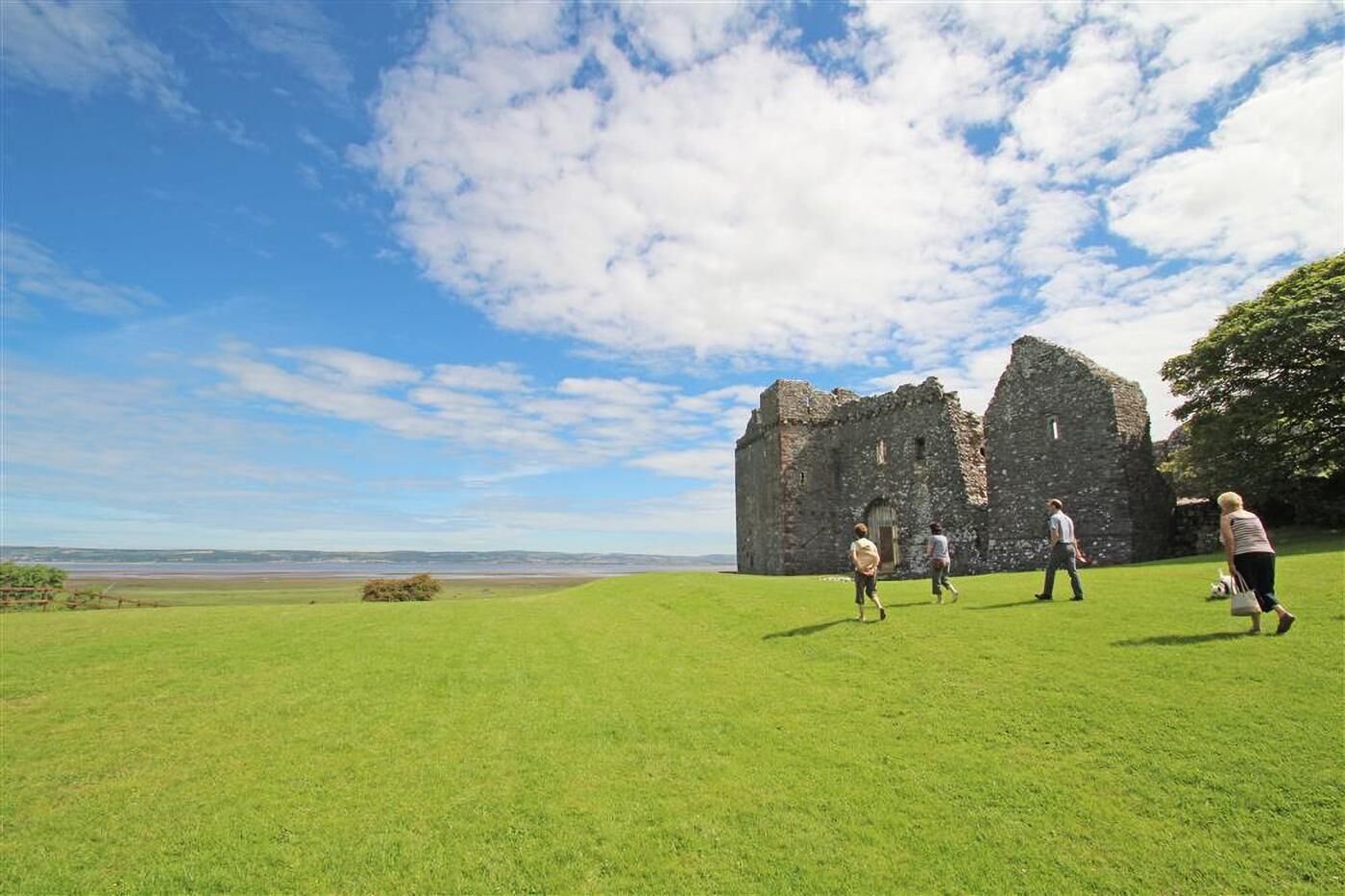 A historic stone building with a grassy field in front, under a clear sky.