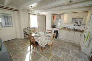 A dining area with a table set for four, a kitchen with white cabinets, and a window with curtains.