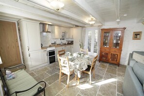 A spacious kitchen with white cabinetry, a dining table set for four, and a built-in oven. - 3 Bed in Swansea (oc-hh405) (Llanmadoc)