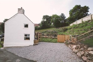 A white house with two windows, a gravel driveway, and a wooden fence. - 3 Bed in Swansea (oc-hh405) (Llanmadoc)