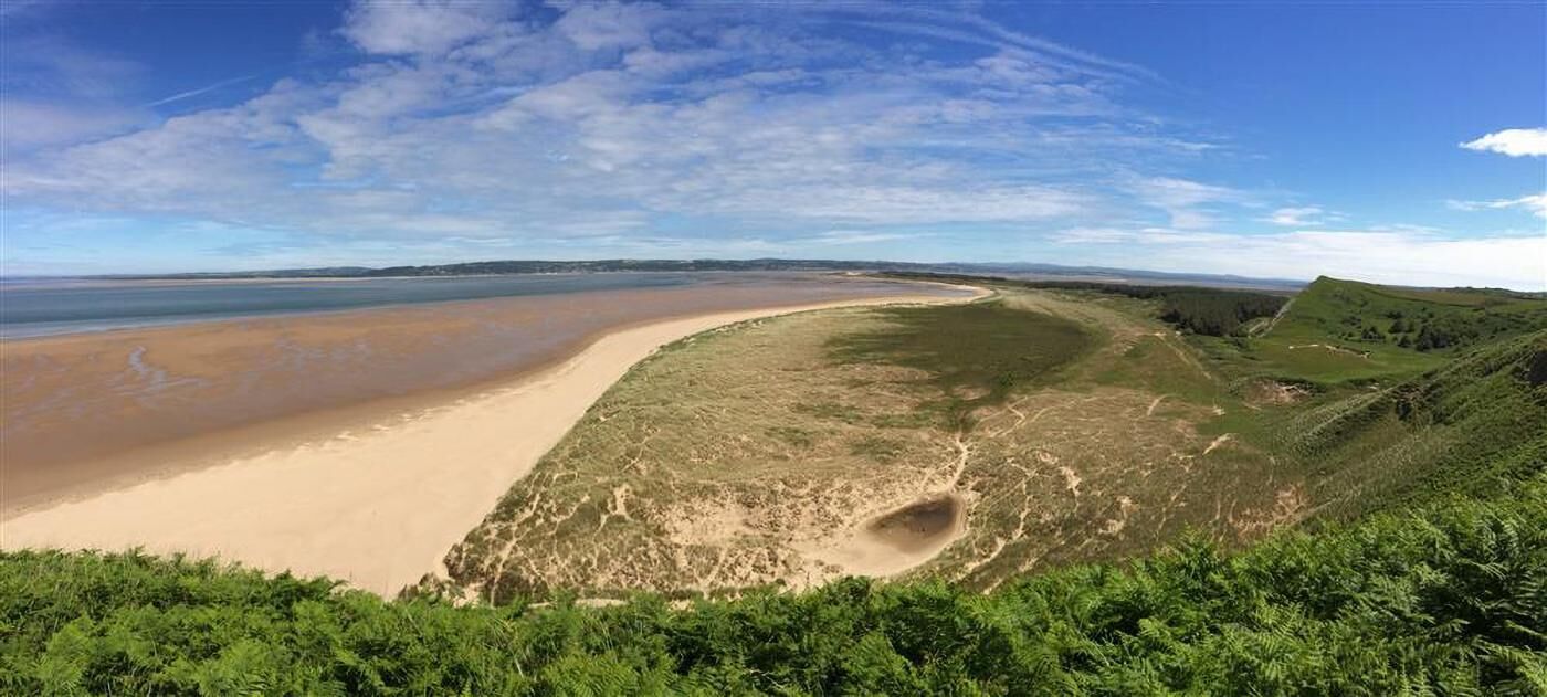 Paisagem costeira com uma praia arenosa, dunas gramadas e céu claro.