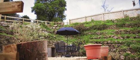 An outdoor patio with a wooden deck, a table with chairs, a blue umbrella, and potted plants.
