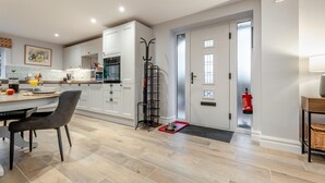 A modern kitchen with white cabinets, a dining area with a table and chairs, and a fire extinguisher near the door. - 2 Bed in Alnwick (oc-e34719) (Alnwick)