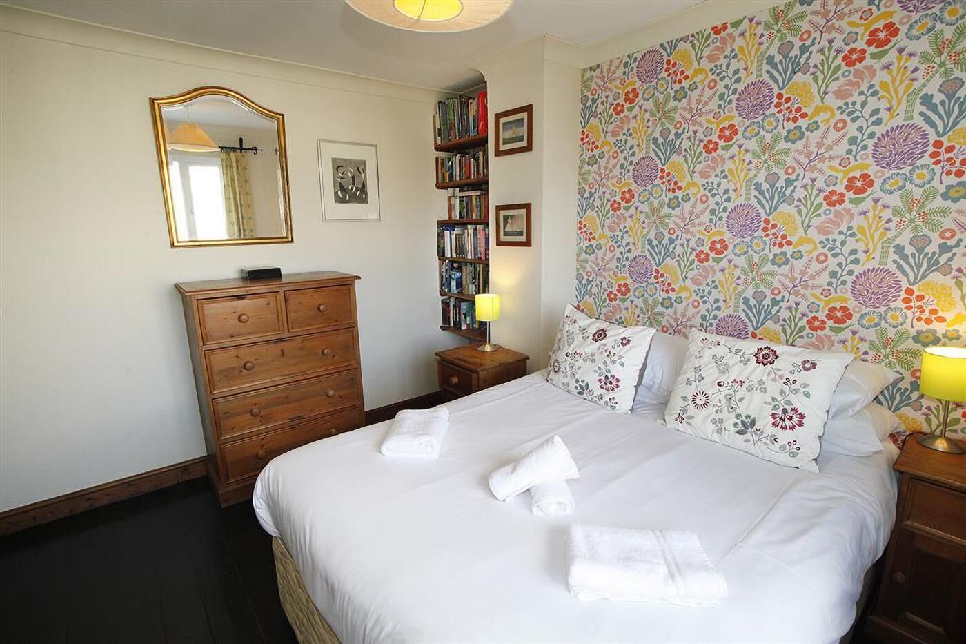 A bedroom with a bed, dresser, bookshelves, and a floral wallpaper.