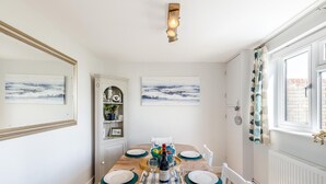 Een eetruimte met een houten tafel voor zes personen, witte wanden en twee kunstwerken erboven.