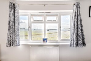 Ein Zimmer mit einem großen Erkerfenster mit Blick auf einen Strand, einem gerahmten Bild auf der Fensterbank und einem weißen Heizkörper darunter.