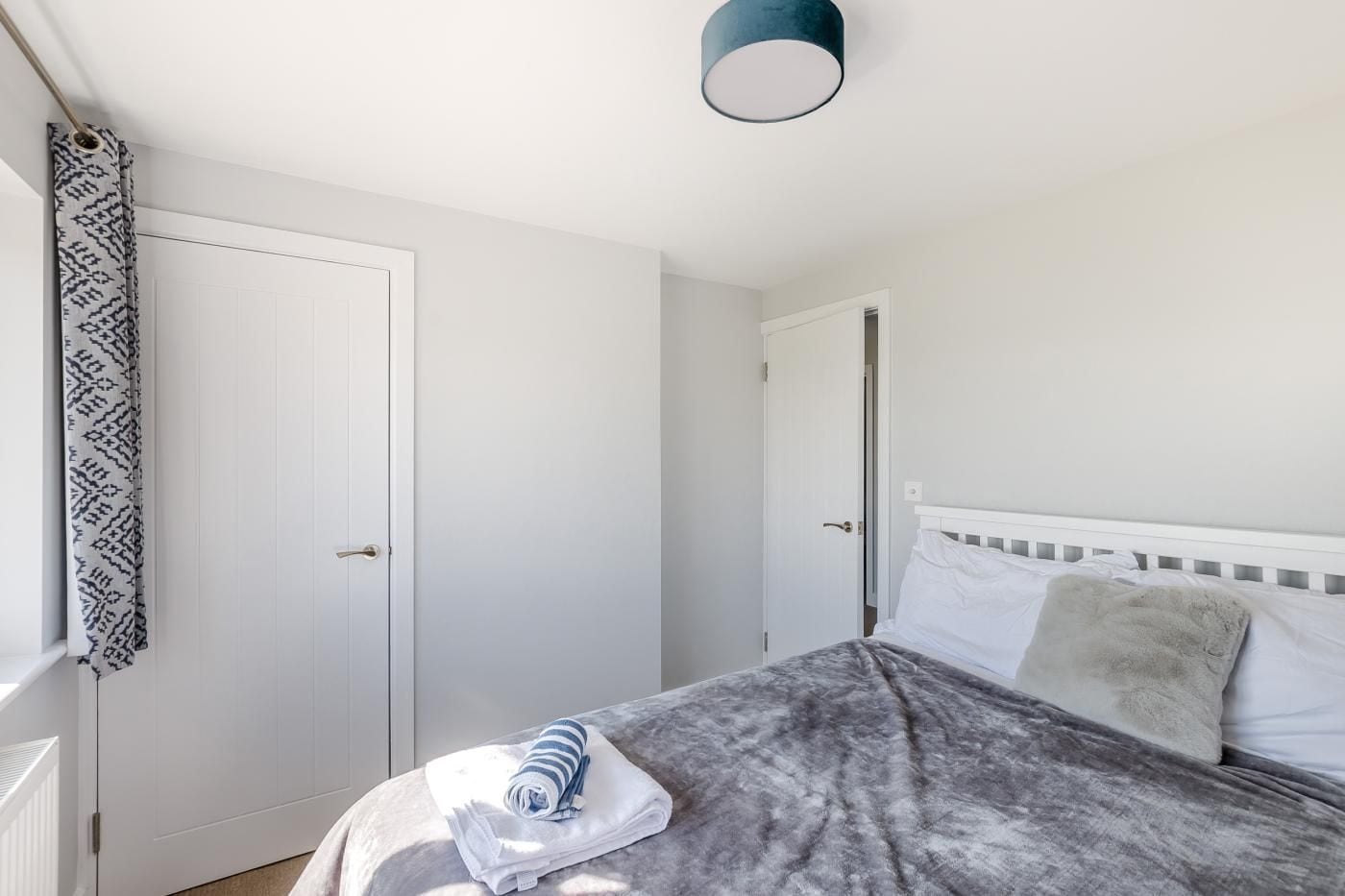 Un dormitorio con cama, una puerta blanca y una ventana con cortina estampada.