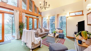 A spacious room with a large window, a sofa, a chair, a small table, and a television. - 4 Bed in Kelso (oc-t34654) (Kelso)