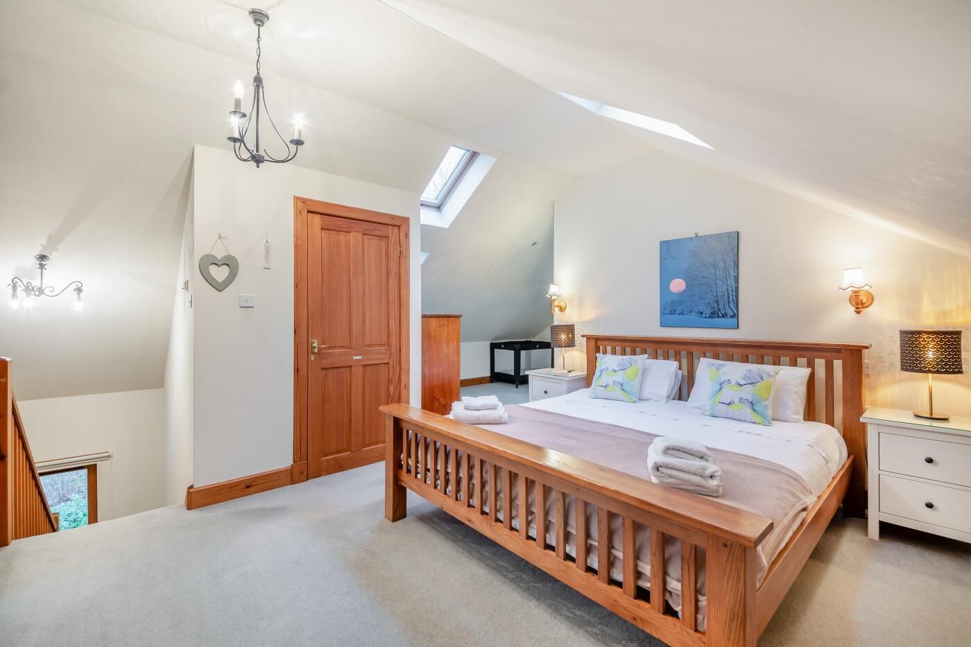 A bedroom with a wooden bed, a nightstand, a desk, a chair, a wardrobe, and a skylight.