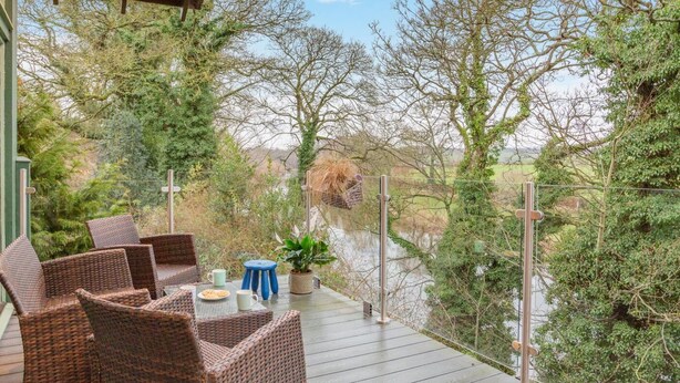 A deck with wicker furniture, a potted plant, and a view of a river and trees. - 4 Bed in Kelso (oc-t34654) (Kelso)